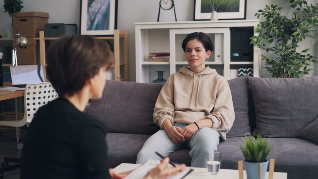 a-woman-sitting-on-a-couch-talking-to-another-woman-m-82pnzgfq4